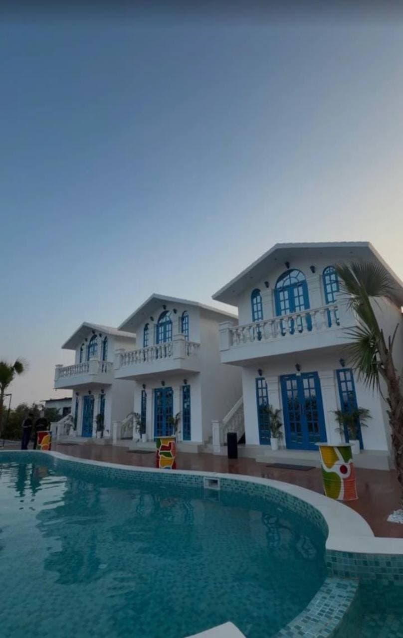 A white property with blue doors and windows beside a swimming pool.